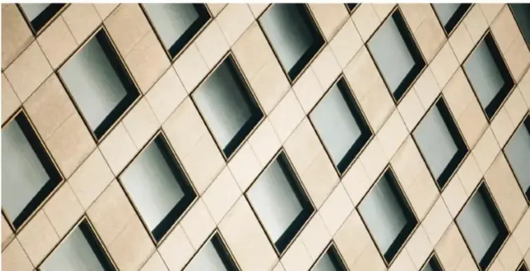 Fotografía de la fachada de un edificio con ventanas rectangulares dispuestas en diagonal sobre muro de piedra clara, ilustración de figuras planas en el entorno.