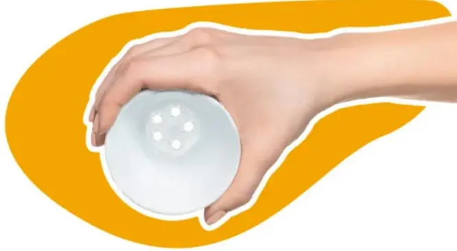 Mano sosteniendo un recipiente blanco redondo con cinco perforaciones pequeñas en la base, sobre un fondo amarillo.