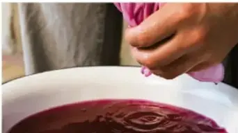 Mano sumergiendo una prenda en un recipiente con tinte rojo intenso.