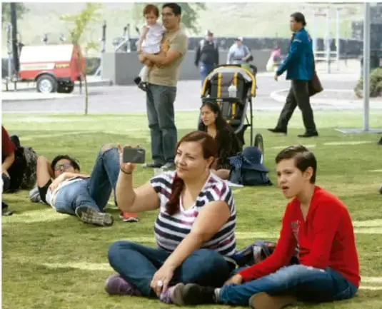 Fotografía de un grupo de personas en un parque: algunas sentadas en el pasto, una tomando una foto con el celular, otras de pie o acostadas, en un ambiente de convivencia comunitaria.