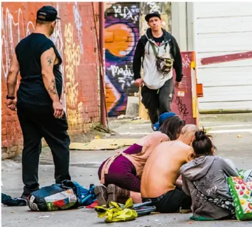 Fotografía de una calle con grafitis donde se observan varias personas sentadas en el suelo y un joven de pie, en una escena que ilustra la exclusión social y el consumo de sustancias en espacios públicos.