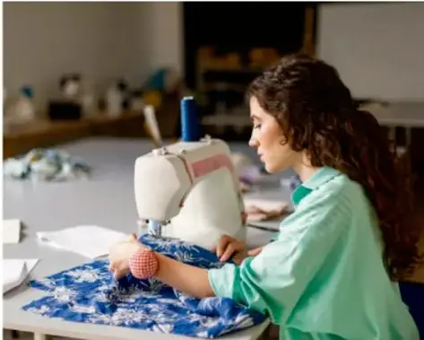Fotografía de una joven utilizando una máquina de coser en un taller textil, ilustrando la relación entre técnica y actividad productiva comunitaria.