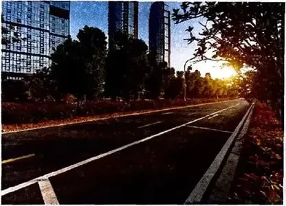 Calle amplia de una ciudad con edificios altos, árboles y luz del amanecer.