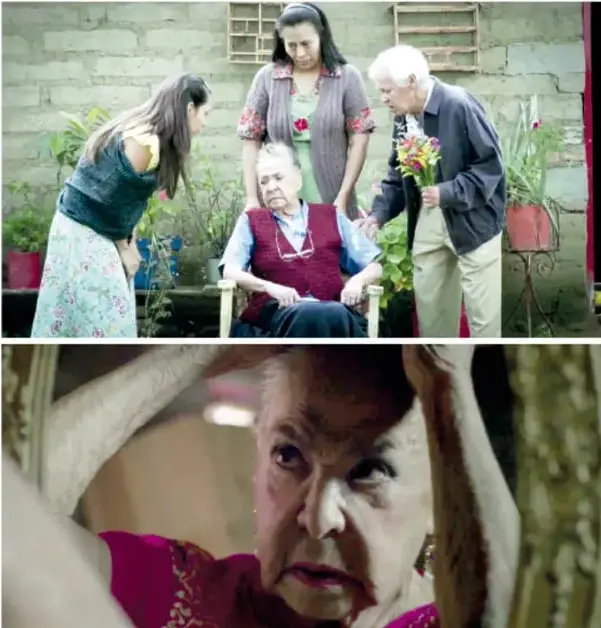 Fotograma del cortometraje: Ramona sentada en el patio, rodeada de su familia y vecinos que llegan a despedirse.