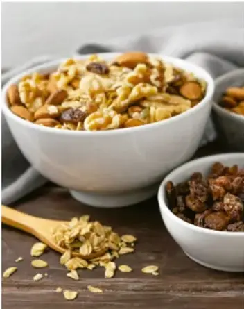 Fotografía de un tazón con cereal de maíz y otro con pasas, sobre una mesa de madera.