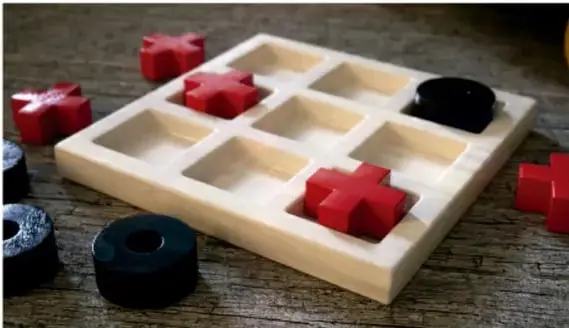 Fotografía de un juego de mesa tradicional de tres en línea, con piezas rojas y negras sobre un tablero de madera.