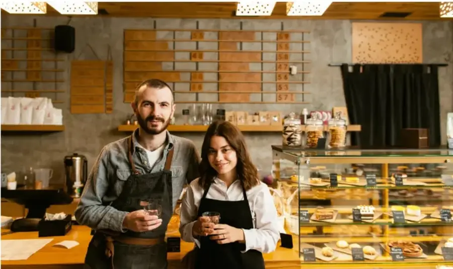 Fotografía de un hombre y una mujer con delantales en una cafetería/panadería, representando a emprendedores de un negocio pequeño.