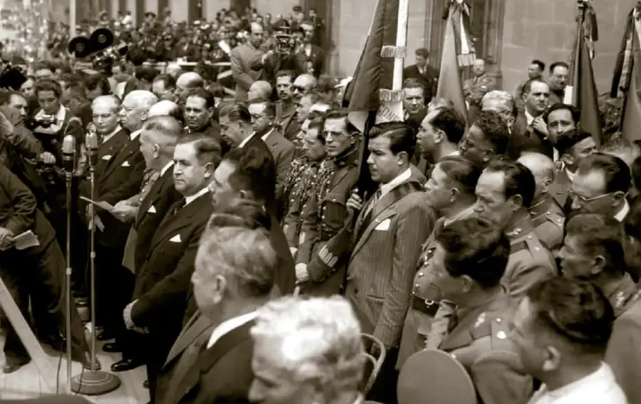 Fotografía histórica en sepia del 'Día de la unidad nacional' (15 de septiembre de 1942) con políticos y militares mexicanos de pie junto a banderas: Pascual Ortiz Rubio, Abelardo L. Rodríguez, Plutarco Elías Calles, Manuel Ávila Camacho, Lázaro Cárdenas, Emilio Portes Gil, Adolfo de la Huerta y Heriberto Jara.