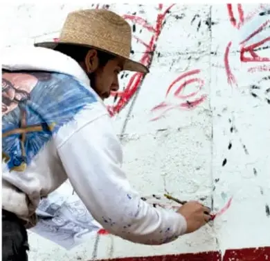 Persona con sombrero de paja pintando o interveniendo un muro con gráfica, ejemplo de arte público o comunitario.
