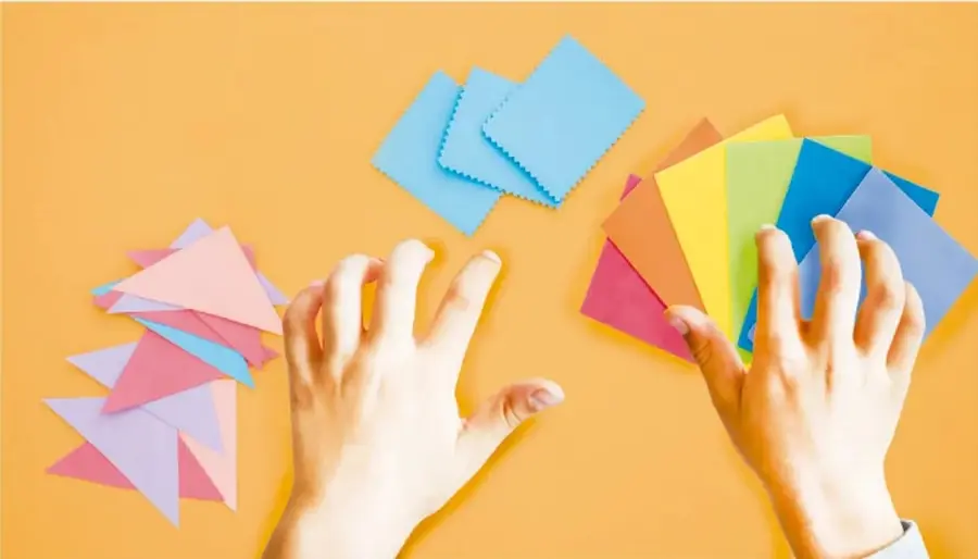 Fotografía de dos manos manipulando figuras geométricas de colores (triángulos y cuadrados) sobre fondo naranja