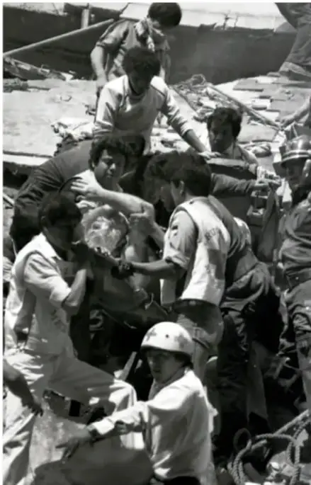 Fotografía en blanco y negro de socorristas y civiles rescatando a una persona de los escombros de un edificio derrumbado tras el sismo de 1985.