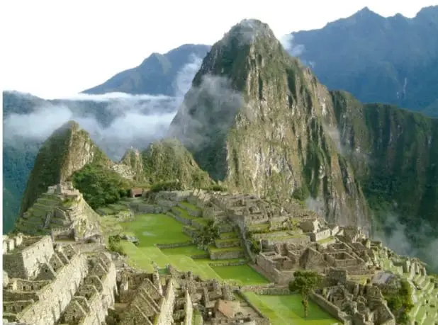 Vista de las ruinas de Machu Picchu entre montañas andinas cubiertas de vegetación y neblina.