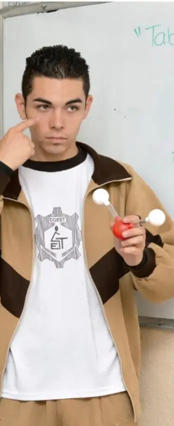 Fotografia de un estudiante varon de secundaria en el aula, senalando con el dedo y sosteniendo un modelo molecular de esferas de colores (rojo y blanco), con pizarra blanca al fondo.