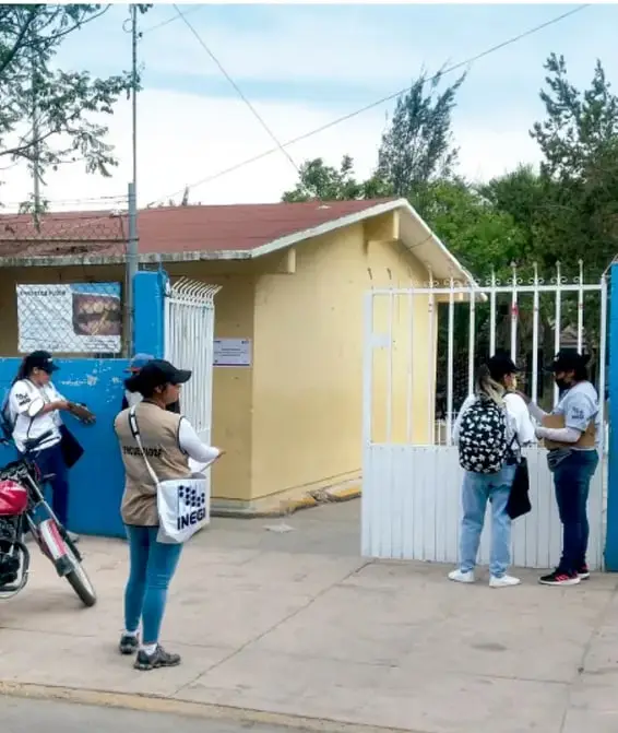 Fotografía de personal del INEGI entrevistando a personas frente a una escuela durante una jornada de levantamiento de datos censales.