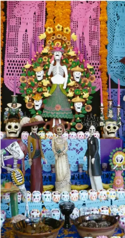 Altar de Día de Muertos con una figura central de La Catrina, rodeada de papel picado, flores de cempasúchil, velas y calaveras decoradas.