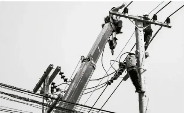 Fotografía en blanco y negro de trabajadores reparando postes y cables eléctricos.