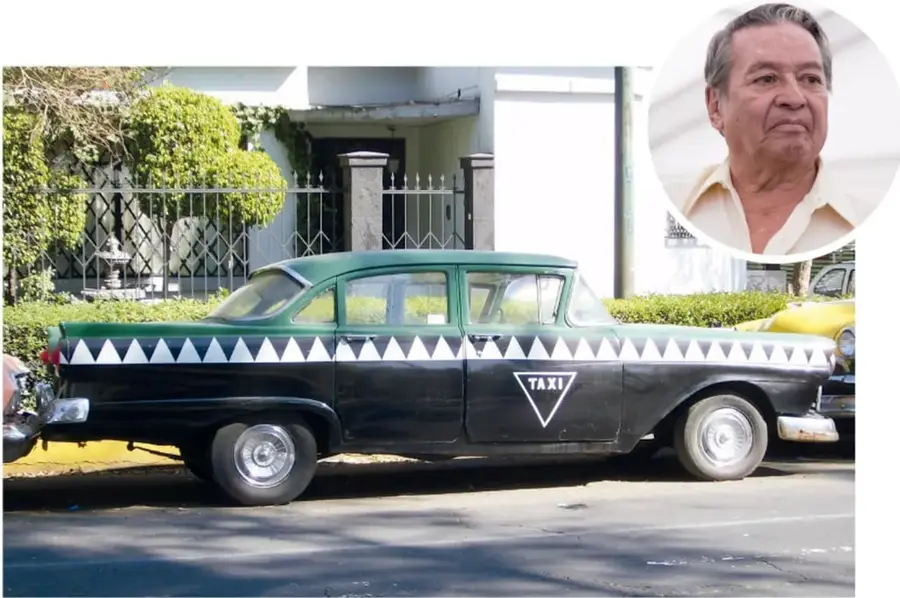 Automóvil clásico verde con franja de triángulos blancos y negros, con la palabra TAXI en un triángulo invertido en la puerta. Está estacionado frente a una casa con reja y vegetación.