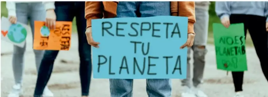 Fotografía de jóvenes en una marcha ambiental que cargan carteles hechos a mano; el central azul dice 'RESPETA TU PLANETA', y se ven otros carteles verdes y naranjas alusivos al cuidado del planeta.