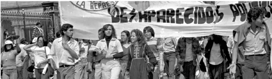Fotografía en blanco y negro de una marcha con una manta que dice 'DEZAPARECIDOS POLÍTICOS'.