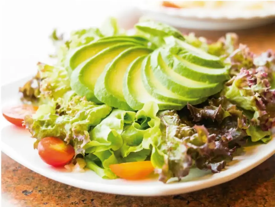 Fotografía de una ensalada con lechuga, rodajas de aguacate y jitomates cherry, que representa alimentos frescos y coloridos.