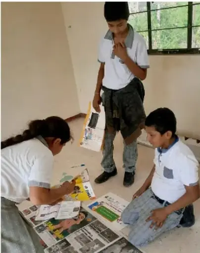 Fotografía de tres estudiantes en el aula trabajando con periódicos y revistas sobre el piso, elaborando materiales para su proyecto.