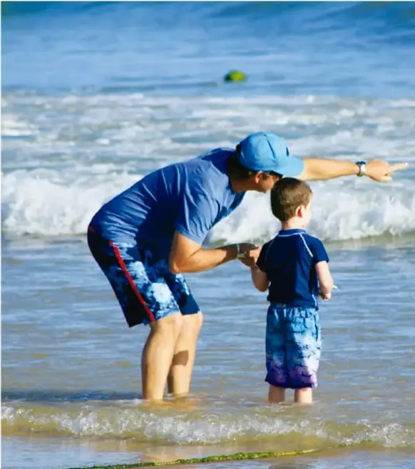 Fotografía de un adulto y un niño de pie en el mar, el adulto señala hacia el horizonte; contexto de aprendizaje en familia.