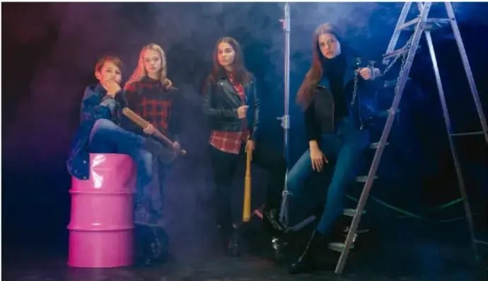 Fotografía de cuatro jóvenes en un set con humo, escalera y barril rosa, representando una producción audiovisual o performativa.