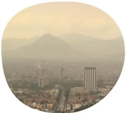 Fotografía circular de una ciudad con neblina o esmog bajo montañas, ilustrando la contaminación del aire.