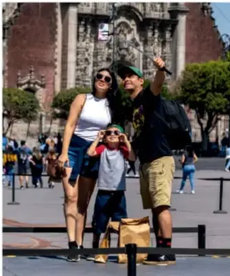 Fotografía de una familia (madre, padre e hijo) tomándose una selfie en una plaza pública, con una iglesia al fondo. Representa la vida comunitaria actual.