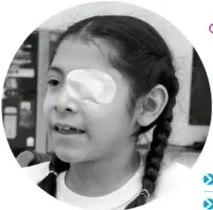Fotografía en blanco y negro de una niña de trenzas con etiqueta adhesiva en la frente, sonriendo.
