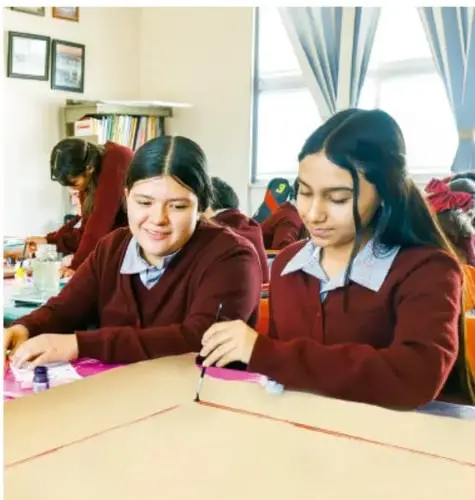 Fotografía de estudiantes de telesecundaria en uniforme, trabajando en equipo en un salón con materiales sobre la mesa, elaborando su cuadro con columnas.
