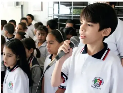 Niño hablando por micrófono durante una exposición frente a sus compañeros.
