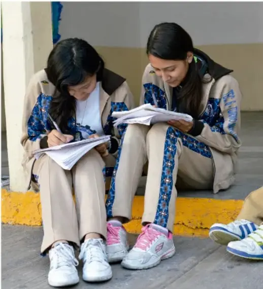 Fotografía de dos estudiantes sentadas en el piso escribiendo y leyendo en sus cuadernos durante una actividad escolar.