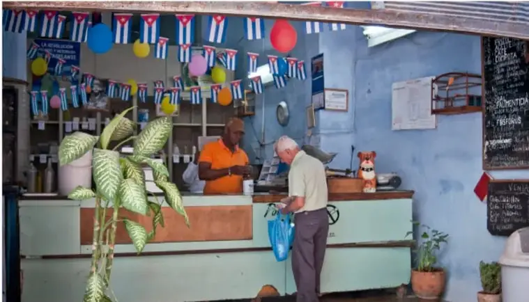 Interior de una tienda o comercio con banderas cubanas, un dependiente y un cliente.