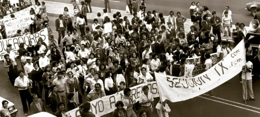 Fotografía en blanco y negro de una multitud de maestros de la CNTE manifestándose en una calle circa 1989, portando pancartas con consignas sobre seguridad social y contra recortes; procede del Archivo Gráfico de El Nacional, Acervo INEHRM.