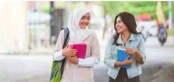Dos estudiantes conversan mientras llevan materiales escolares. La imagen representa que la educación laica incluye tanto a personas religiosas como a quienes no practican una religión.