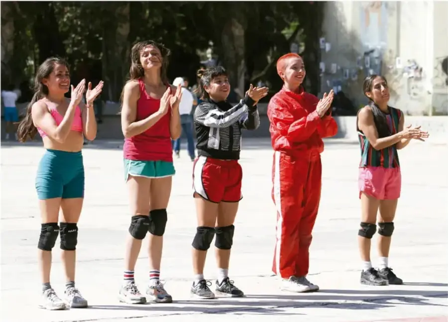 Fotografía de cinco jóvenes en ropa deportiva y rodilleras aplaudiendo en una plaza al aire libre, ilustrando la acción motriz colectiva.