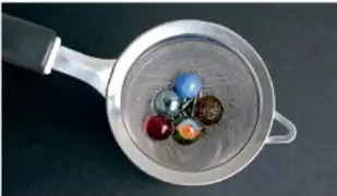 Colador metálico de cocina con canicas y partículas sólidas retenidas.