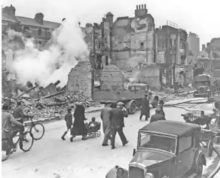 Fotografía histórica en blanco y negro de una ciudad en ruinas tras un bombardeo, con civiles, ciclistas y automóviles entre los escombros, ilustrando los efectos de la guerra en la vida cotidiana.