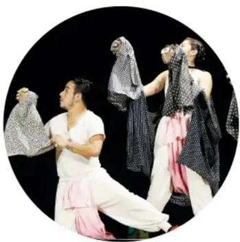 Fotografía de danza escénica: bailarines con vestuarios amarillos, naranjas y verdes ante un telón azul con volcanes y una pirámide pintados.