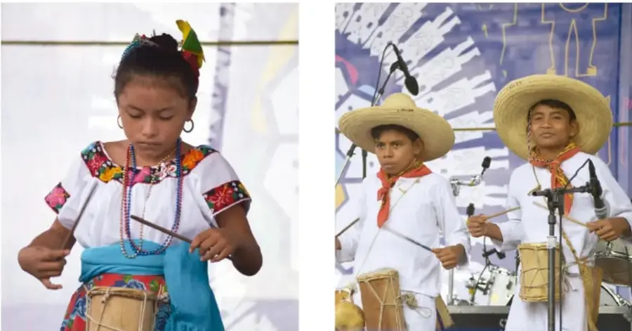 Niña con blusa bordada y falda azul toca un tambor durante una presentación.