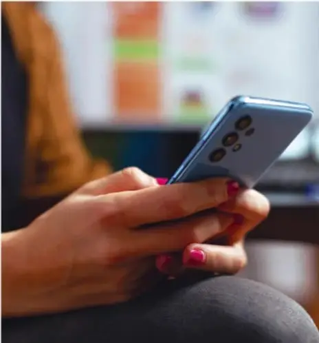 Fotografía de una persona sosteniendo un teléfono inteligente con ambas manos, con fondo desenfocado, que ilustra el uso de dispositivos móviles y redes sociales.