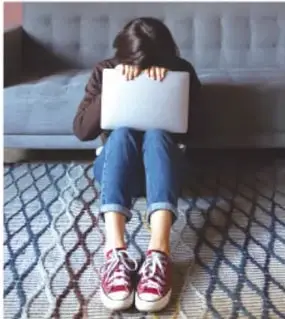 Persona sentada en el suelo usando una laptop, con la cabeza agachada, en una habitación con alfombra.