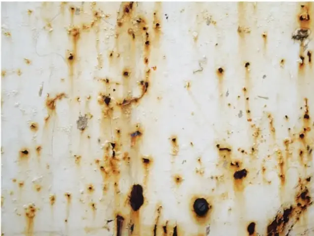 Fotografía de una superficie metálica blanca con manchas de óxido color marrón, mostrando el proceso de corrosión del hierro.