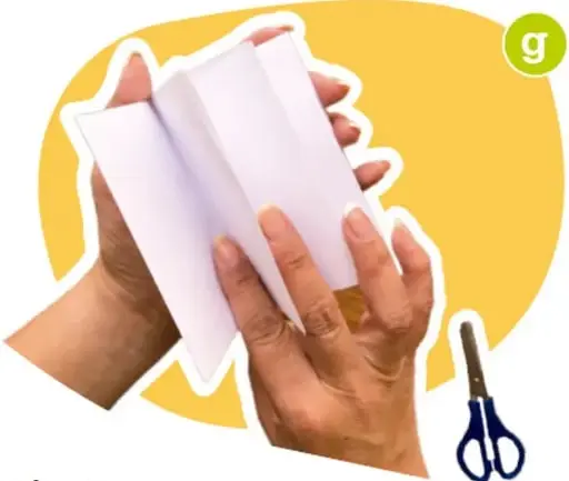 Manos sosteniendo una hoja de papel doblada en secciones, con tijeras al lado.
