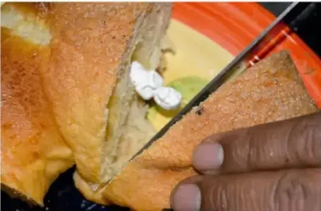 Fotografía de manos cortando una rebanada de pan de muerto sobre un plato.