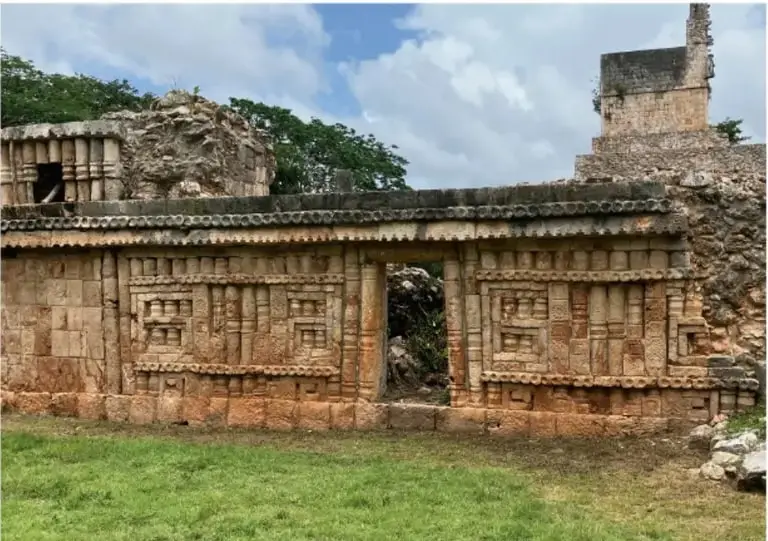 Fotografía del Edificio del grupo de Palacio en Labná, Yucatán: fachada larga con frisos estilo Puuc, Mirador al fondo, pastizal y árboles; encuadre blanco sobre fondo magenta.