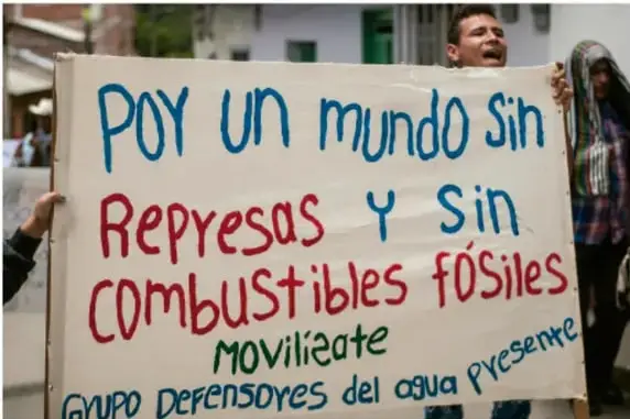 Fotografía de manifestantes sosteniendo una pancarta que dice: "POY un mundo sin Represas y sin Combustibles fósiles. Movízate. Grupo Defensores del agua presente".