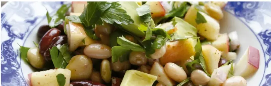 Fotografía de un platillo con frijoles blancos, jitomate, cebolla, cilantro y trozos de fruta o verdura, servido en un plato decorado con motivos azules.