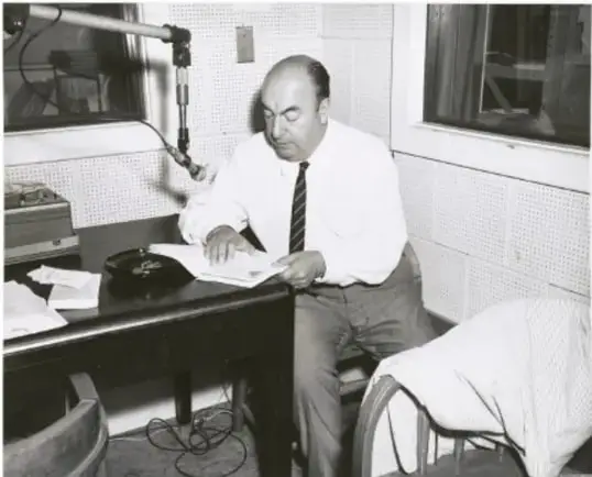 Fotografía en blanco y negro de un hombre (aparentemente un escritor o intelectual) sentado en un escritorio de estudio o cabina de radio, escribiendo o revisando documentos junto a un micrófono y equipo de audio.